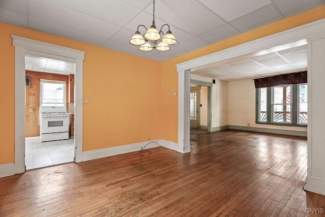 unfurnished dining area featuring baseboards, a drop ceiling, an inviting chandelier, and hardwood / wood-style flooring