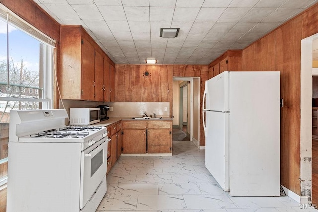 kitchen featuring marble finish floor, light countertops, wood walls, a sink, and white appliances