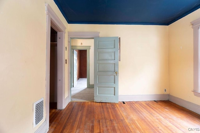 unfurnished room featuring hardwood / wood-style floors, visible vents, and baseboards