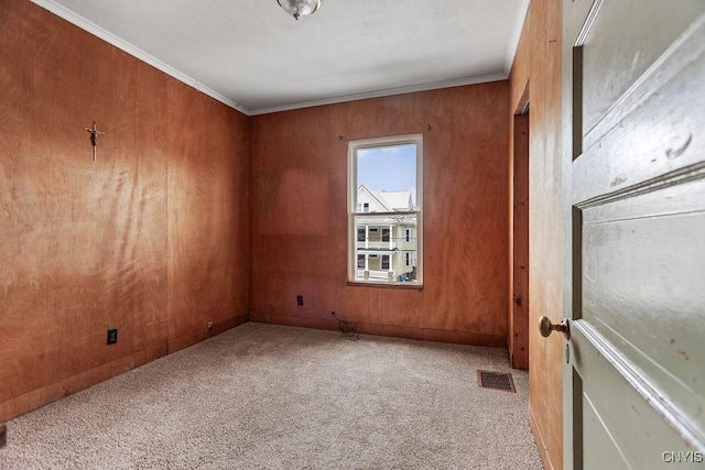 carpeted empty room with wood walls, visible vents, and ornamental molding