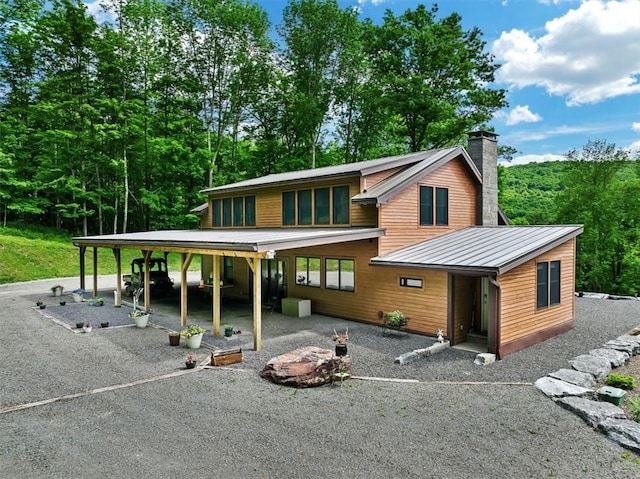 view of front of home featuring driveway, a chimney, metal roof, a standing seam roof, and a carport