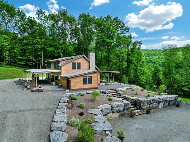 view of front of property with gravel driveway, a chimney, a wooded view, and a carport