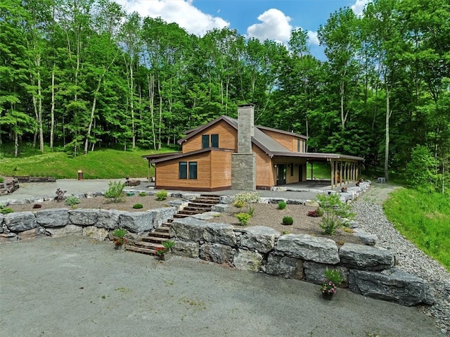 view of home's exterior with a carport, a chimney, and a wooded view