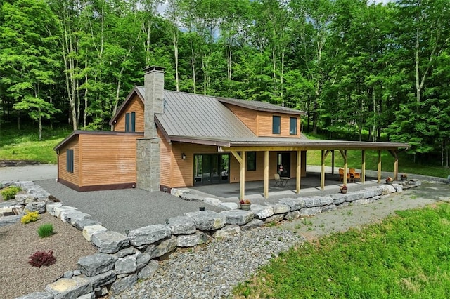 view of front of property featuring a patio area, a chimney, metal roof, and a standing seam roof