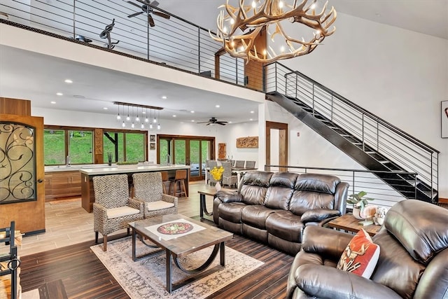 living area featuring recessed lighting, ceiling fan with notable chandelier, a high ceiling, wood finished floors, and stairs