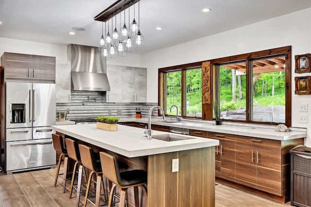 kitchen featuring light countertops, high quality fridge, wall chimney range hood, a sink, and modern cabinets