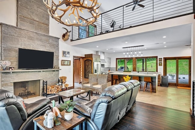 living room with ceiling fan with notable chandelier, a wealth of natural light, a stone fireplace, and wood finished floors