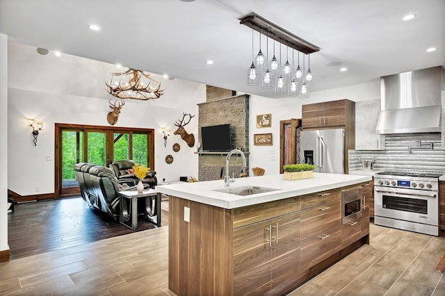 kitchen with appliances with stainless steel finishes, open floor plan, a sink, and wall chimney exhaust hood