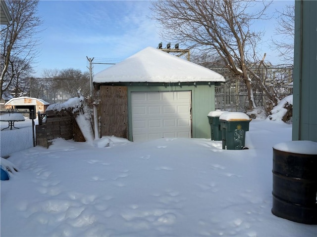 snow covered garage featuring a garage and fence