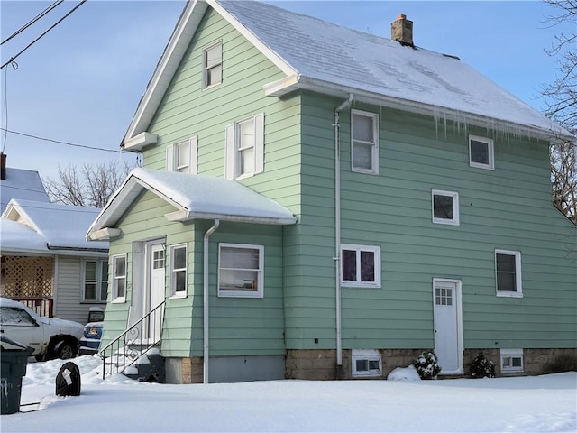 snow covered property featuring a shingled roof, entry steps, and a chimney