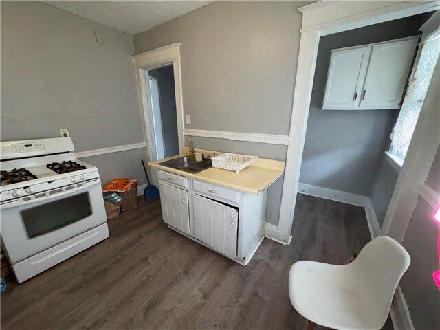 kitchen with a sink, baseboards, white cabinets, white range with gas cooktop, and dark wood-style floors