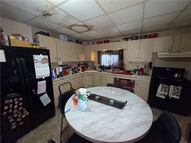 kitchen with a paneled ceiling, under cabinet range hood, tile counters, and freestanding refrigerator