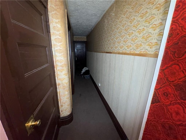 corridor with a wainscoted wall, a textured ceiling, and wallpapered walls