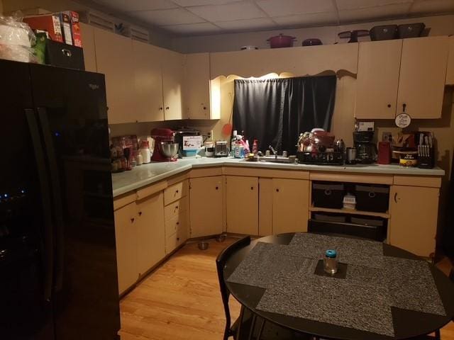 kitchen with a drop ceiling, a sink, light wood-style floors, light countertops, and black refrigerator with ice dispenser