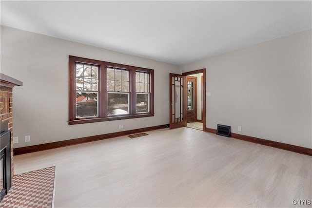 unfurnished living room featuring light wood-type flooring, a brick fireplace, visible vents, and baseboards