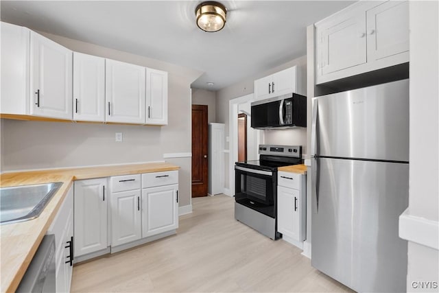 kitchen with appliances with stainless steel finishes, wood counters, light wood-style flooring, and white cabinetry