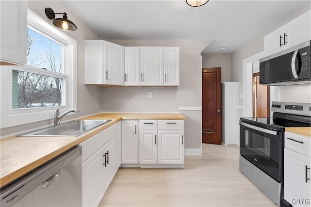 kitchen featuring appliances with stainless steel finishes, light wood-style floors, white cabinets, and a sink