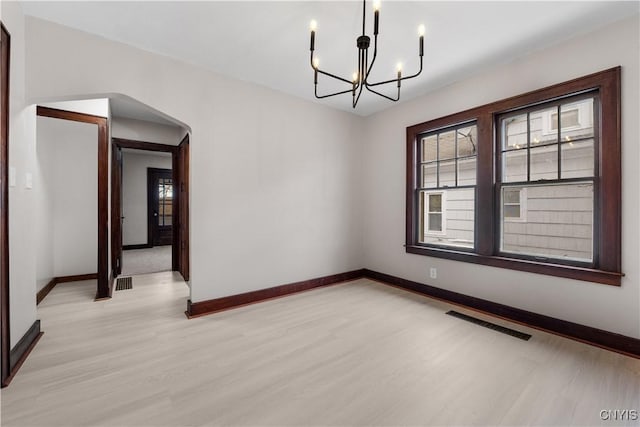 unfurnished room featuring light wood finished floors, plenty of natural light, visible vents, and arched walkways