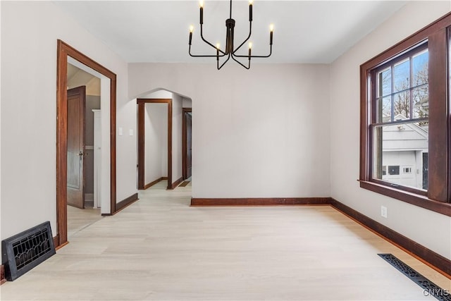 unfurnished dining area with arched walkways, light wood-style flooring, visible vents, baseboards, and an inviting chandelier