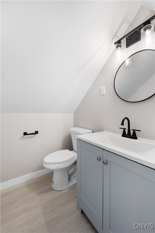 bathroom featuring baseboards, toilet, wood finished floors, vaulted ceiling, and vanity