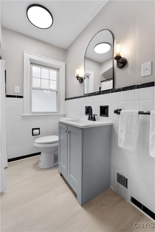 bathroom with toilet, a wainscoted wall, visible vents, vanity, and tile walls