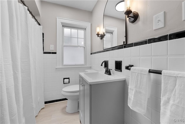 full bath with curtained shower, toilet, a wainscoted wall, vanity, and tile walls