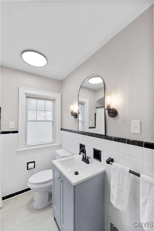 bathroom featuring tile walls, wainscoting, vanity, and toilet