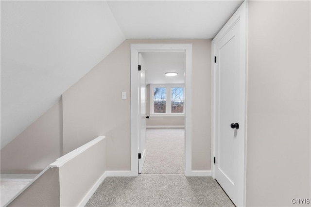 hallway with an upstairs landing, carpet flooring, vaulted ceiling, and baseboards