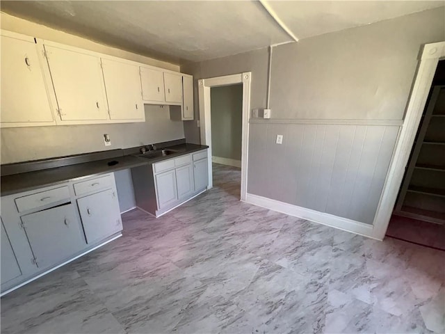 kitchen featuring marble finish floor, dark countertops, white cabinetry, a sink, and wainscoting