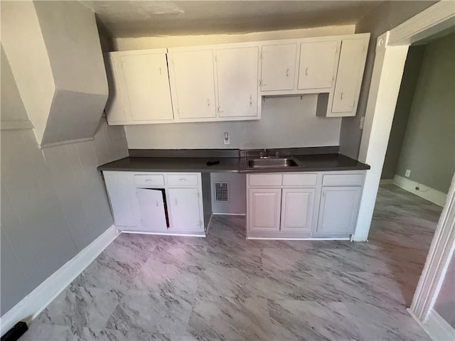 kitchen with visible vents, dark countertops, marble finish floor, white cabinetry, and a sink