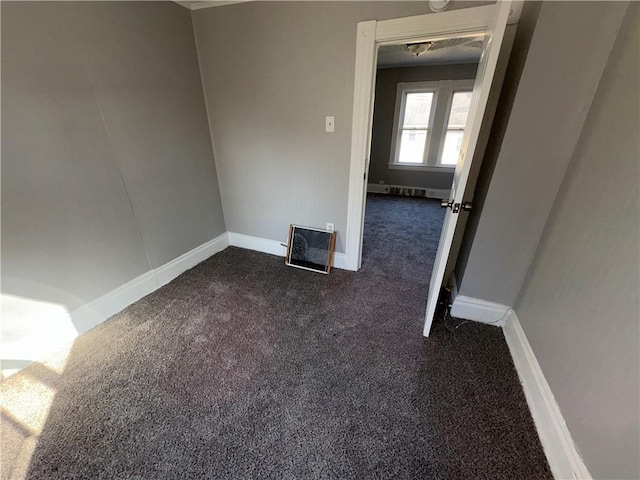 spare room featuring baseboards and dark carpet