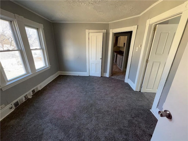 unfurnished bedroom with a textured ceiling, dark colored carpet, and crown molding