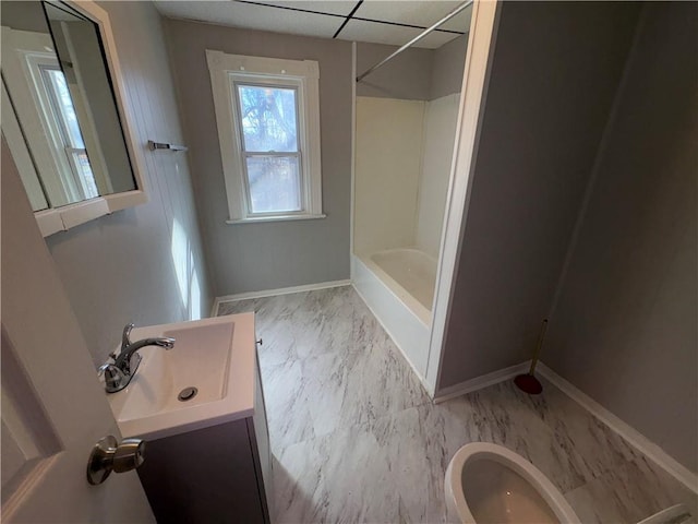 bathroom with a drop ceiling, vanity, baseboards, marble finish floor, and washtub / shower combination