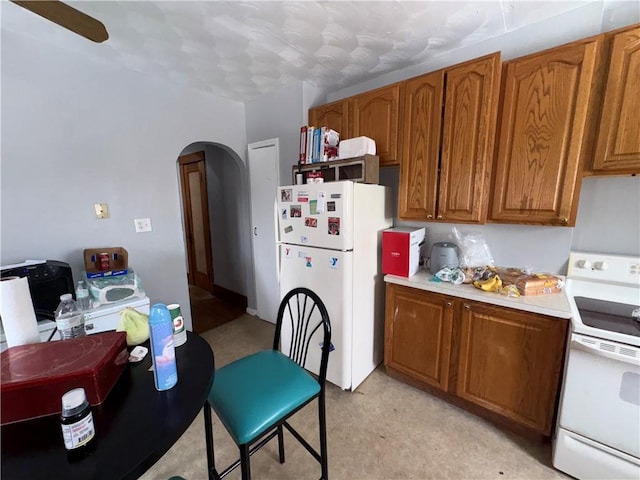 kitchen with arched walkways, white appliances, light countertops, and brown cabinetry