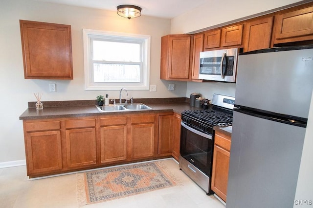 kitchen featuring appliances with stainless steel finishes, brown cabinetry, dark countertops, and a sink