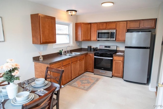 kitchen featuring dark countertops, appliances with stainless steel finishes, brown cabinets, light floors, and a sink