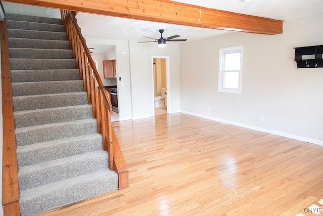 unfurnished living room with light wood-style floors, beamed ceiling, stairway, and baseboards