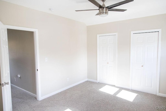 unfurnished bedroom featuring light carpet, ceiling fan, baseboards, and two closets