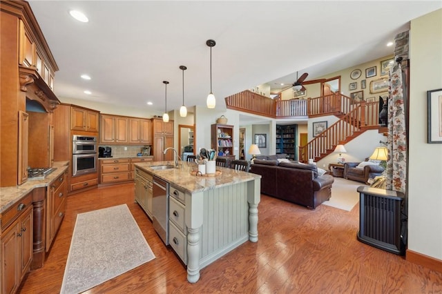 kitchen featuring light wood-style flooring, stainless steel appliances, a sink, light stone countertops, and brown cabinetry