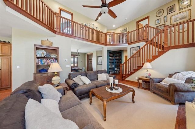 living area featuring a towering ceiling, ceiling fan, stairway, and wood finished floors