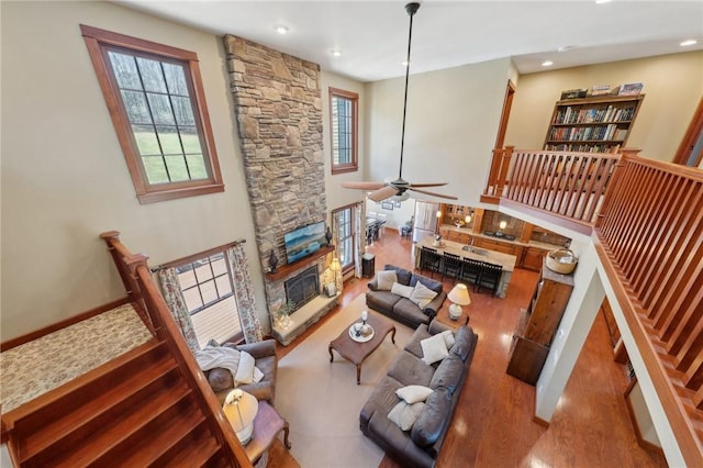 living area featuring recessed lighting, ceiling fan, a stone fireplace, and wood finished floors