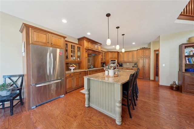 kitchen with appliances with stainless steel finishes, brown cabinets, light stone counters, and wood finished floors