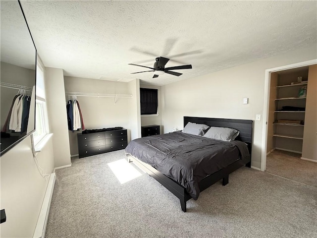 carpeted bedroom with ceiling fan, a textured ceiling, a baseboard heating unit, baseboards, and a closet