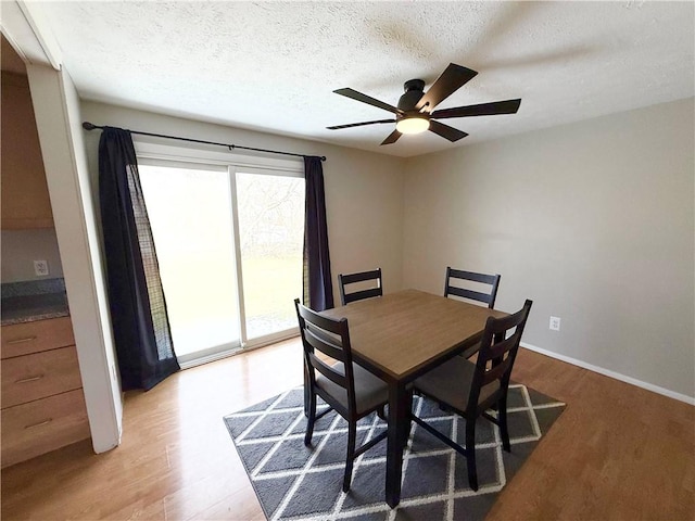 dining room featuring a textured ceiling, light wood finished floors, a ceiling fan, and baseboards