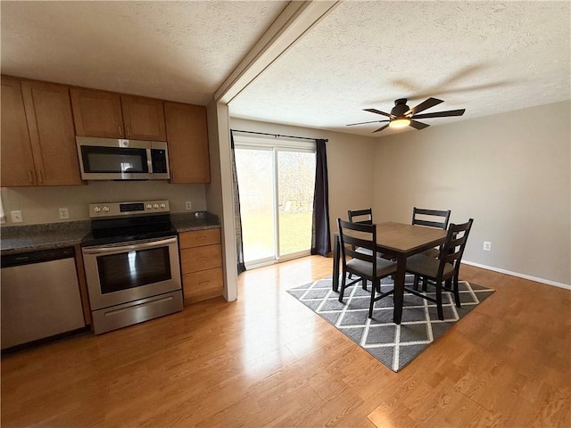 kitchen featuring brown cabinetry, dark countertops, appliances with stainless steel finishes, a textured ceiling, and light wood-style floors