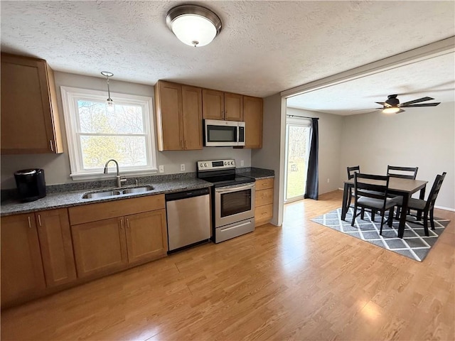 kitchen featuring dark countertops, appliances with stainless steel finishes, brown cabinetry, and a sink