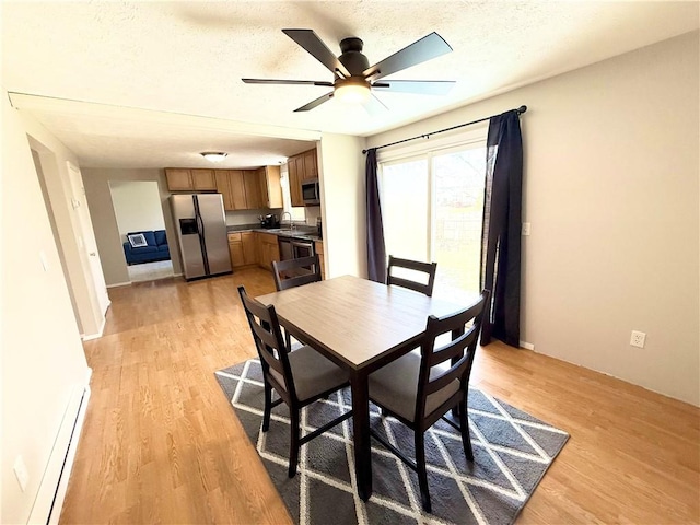 dining room featuring light wood-style flooring, a baseboard heating unit, ceiling fan, and a textured ceiling