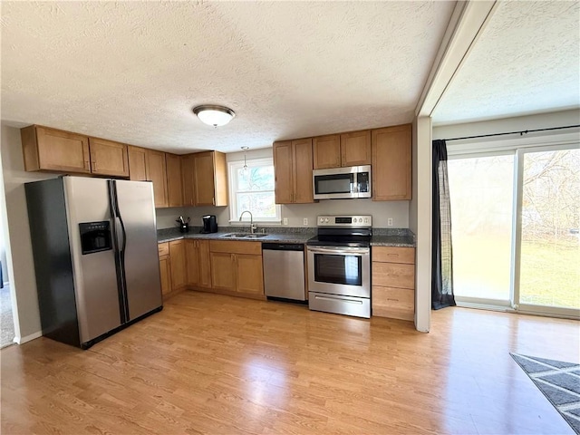 kitchen with stainless steel appliances, light wood-type flooring, a sink, and dark countertops