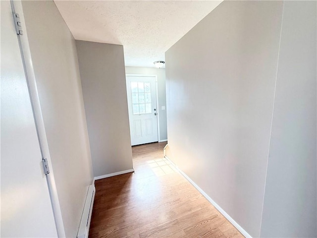 hall with a baseboard heating unit, a textured ceiling, wood finished floors, and baseboards