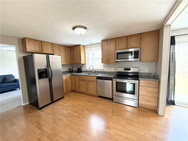 kitchen featuring stainless steel appliances, light wood-style floors, a sink, and dark countertops